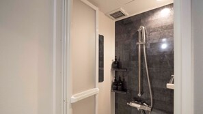 A modern shower with a handheld showerhead and a wall-mounted faucet, a small shelf with toiletries, and a vent above the shower. - R98BB2E_501 / Taito-ku Tokyo (Taito-ku)