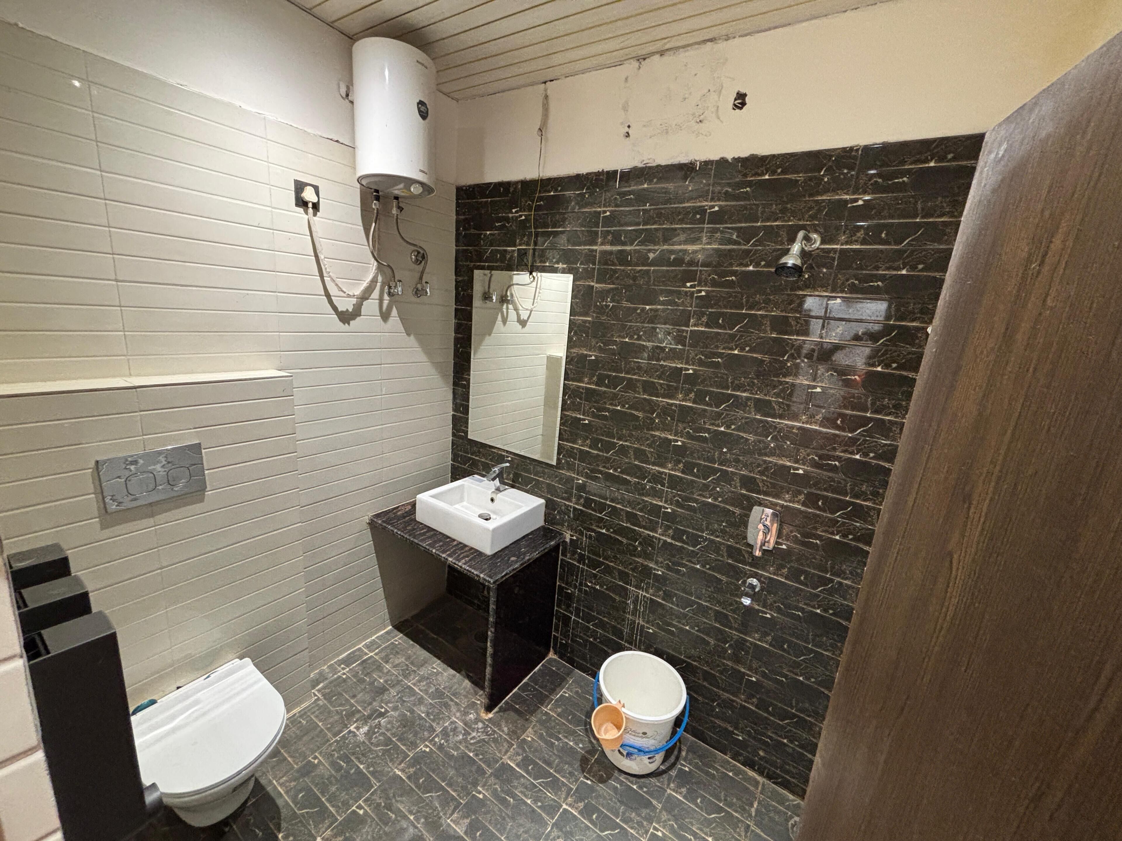 Ein Badezimmer mit einer weißen Toilette, einem Waschbecken mit schwarzer Arbeitsplatte, einem Spiegel und einer Wand mit schwarzen Fliesen.