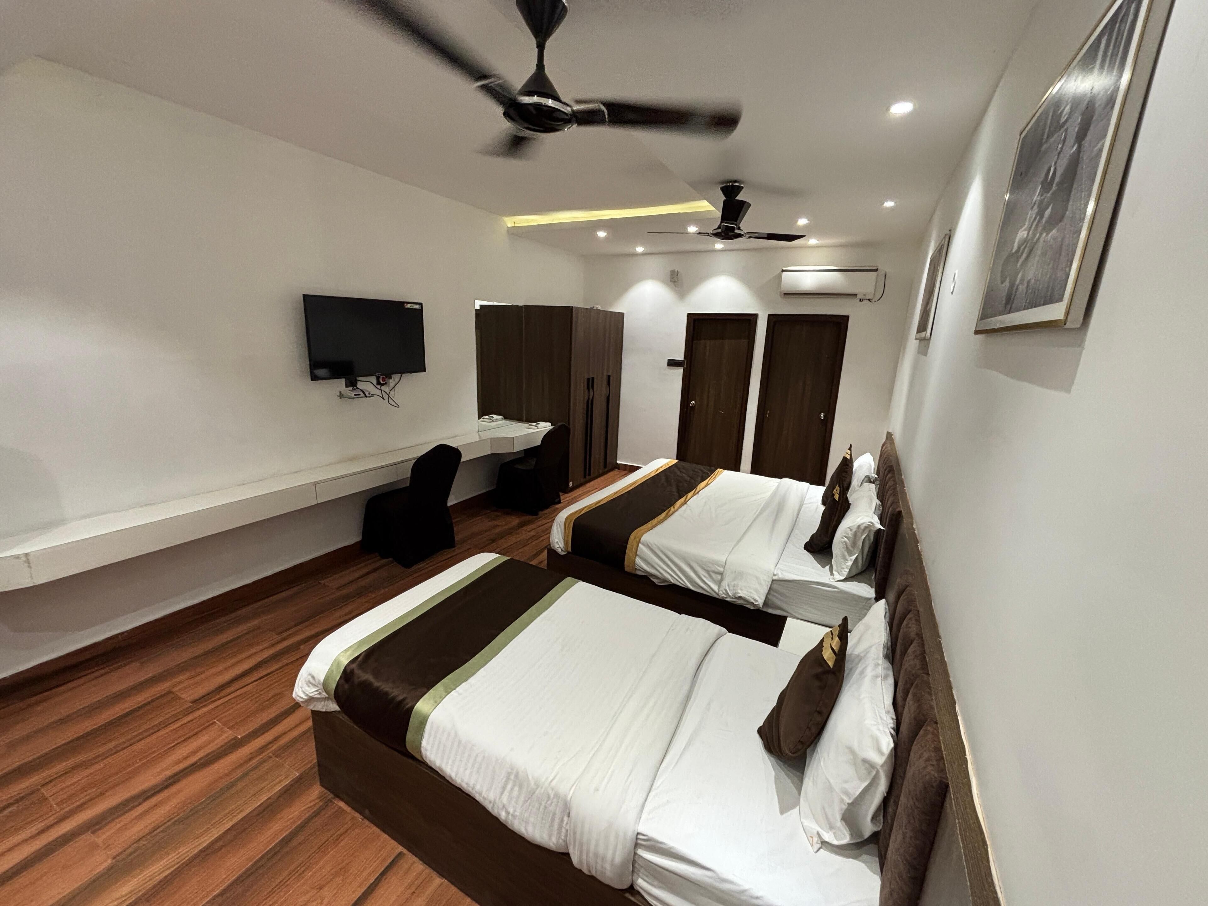 Una habitación de hotel con dos camas, un escritorio, una silla, un televisor y un ventilador de techo.