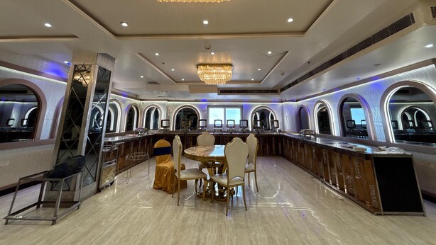 A luxurious dining area with a central round table, elegant chairs, and a large chandelier. - Hotel Citrus (Lucknow)