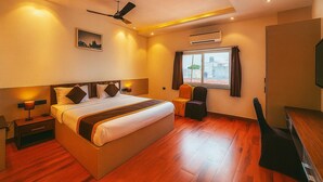 A hotel room with a large bed, a desk, a chair, a ceiling fan, an air conditioning unit, and a window with curtains. - Hotel Citrus (Lucknow)