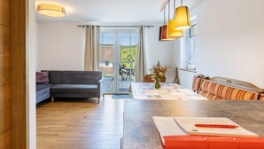Uma sala de estar moderna com sofá, mesa de jantar e vista através de uma porta de vidro.