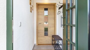 Um corredor estreito com porta de madeira, um banco e uma janela com vista para um prédio de tijolos.