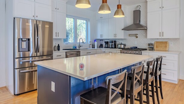 A modern kitchen with white cabinetry, stainless steel appliances, and a central island with bar stools. - Spacious 6BR/5BA - Near DC & Pentagon (Arlington)