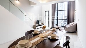 Un espace de repas moderne avec une table en bois dressée pour quatre personnes, un canapé et une grande fenêtre avec des rideaux.