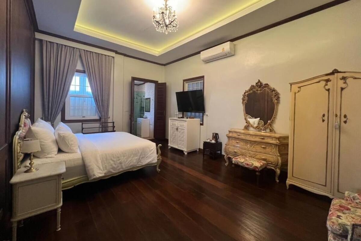 A bedroom with a bed, a dresser, a mirror, and a chandelier.