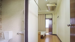 A bathroom with a toilet and sink, a bedroom with a bed and window, and a wooden door. - Suriyart Hotel (Ubon Ratchathani)