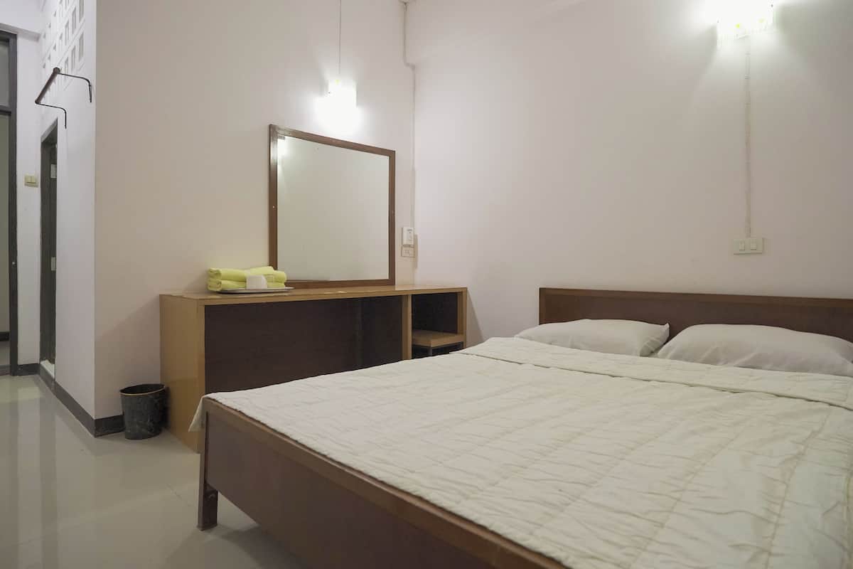 A bedroom with a bed, a bedside table, a mirror, and a wall-mounted light fixture.