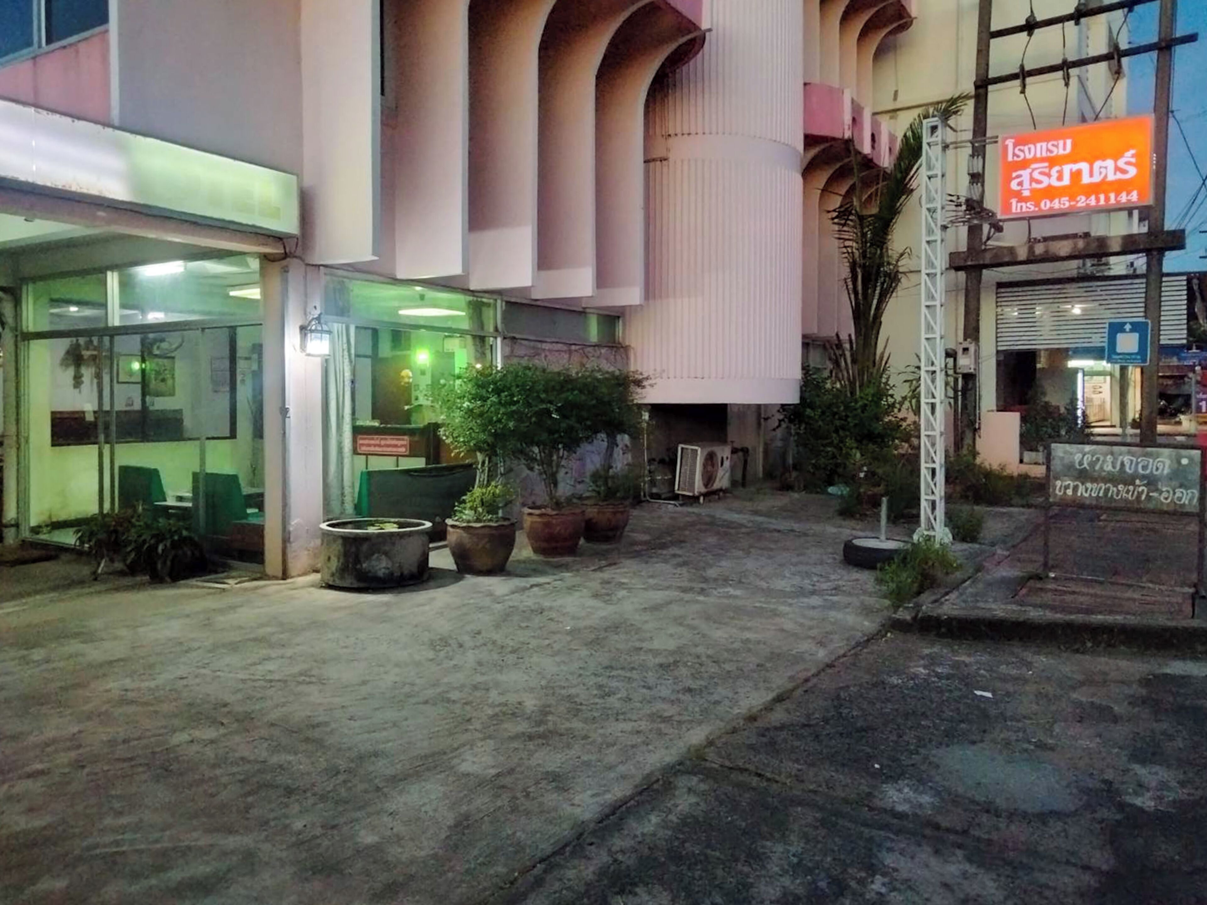 A building with a glass entrance, potted plants, and a sign with a phone number.