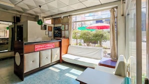 A small, simple room with a reception desk, a sofa, and a table. There are windows with curtains and a view of the street outside. - Suriyart Hotel (Ubon Ratchathani)