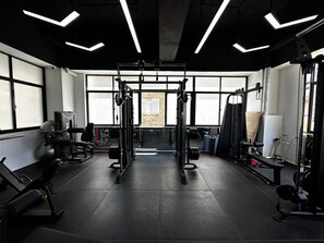 Ett gym med olika typer av träningsutrustning, stora fönster och en stenmur i bakgrunden.