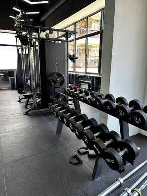 A gym with weightlifting equipment, including dumbbells and a squat rack. - Luxury 1BR in Kilimani- Pool, Gym & Stunning Views (Nairobi)