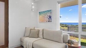 Une pièce chaleureuse avec un canapé beige, un tableau et une vue sur l’océan.