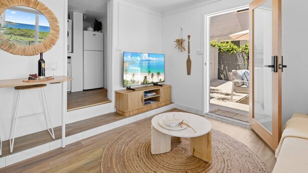 Un salon moderne avec un téléviseur, des meubles en bois, une table ronde et une vue sur l’extérieur.