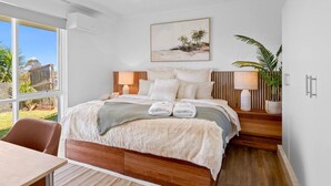 Une chambre moderne avec un grand lit, une tête de lit en bois, des lampes de chevet, une vue sur l’extérieur et un tableau au mur.