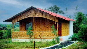 A bamboo house with a red roof, surrounded by lush greenery.
