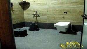 A small, compact bathroom with a wooden wall, a white toilet, and a black pedestal sink.