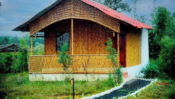 A single-story bamboo structure with a red roof and a covered porch, surrounded by lush greenery.