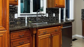 A kitchen with wooden cabinets, a granite countertop, a stainless steel sink, and a dishwasher. - Cozy Corner on Carson (Burney)