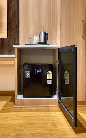 Una cucina compatta con forno a microonde integrato e bollitore, un piccolo frigorifero e un mobile con finitura in legno.