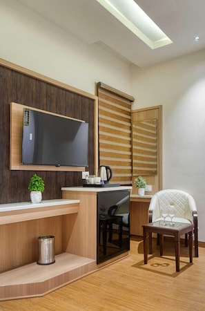 Una cucina moderna con TV integrata, mobili in legno e un piccolo angolo salotto con una sedia e un tavolo.