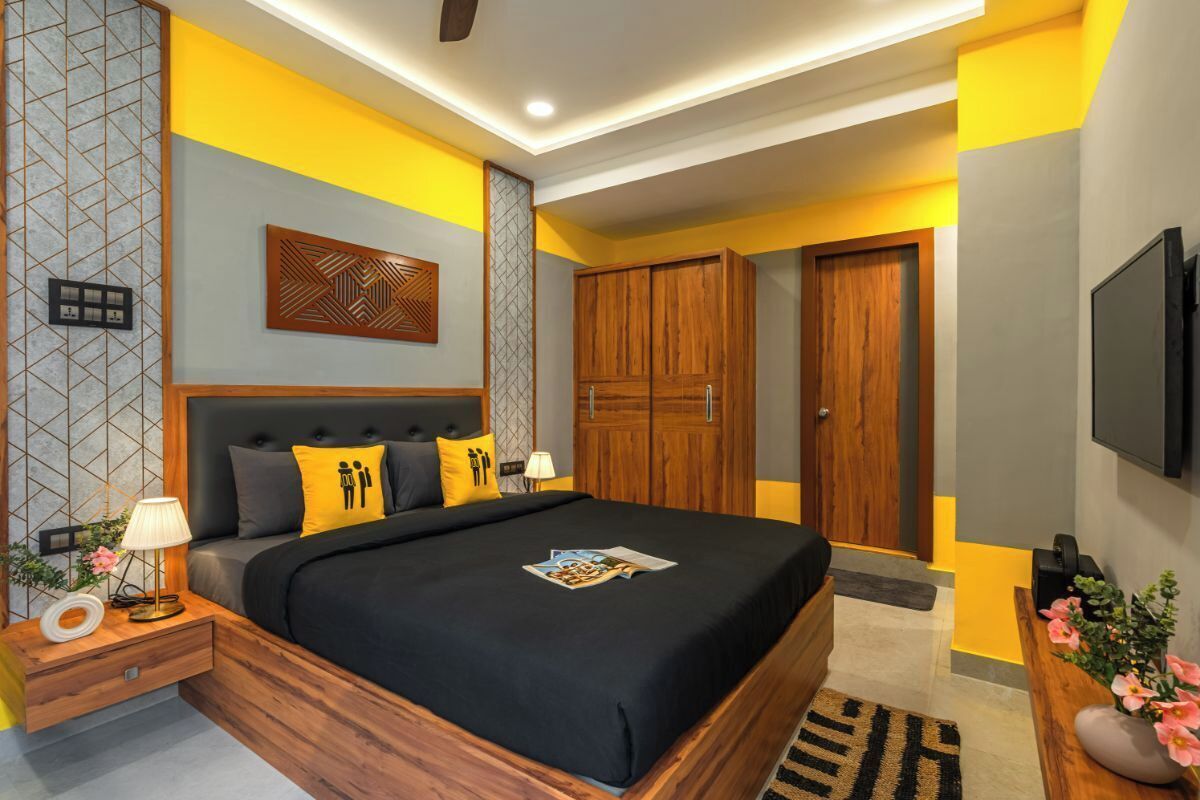 A modern bedroom with a large bed, wooden wardrobe, and a TV mounted on the wall.