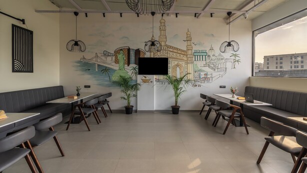 A modern dining area with booths and tables, a mural of a cityscape, and potted plants. - The Hosteller Hyderabad HITEC City (Hyderabad)