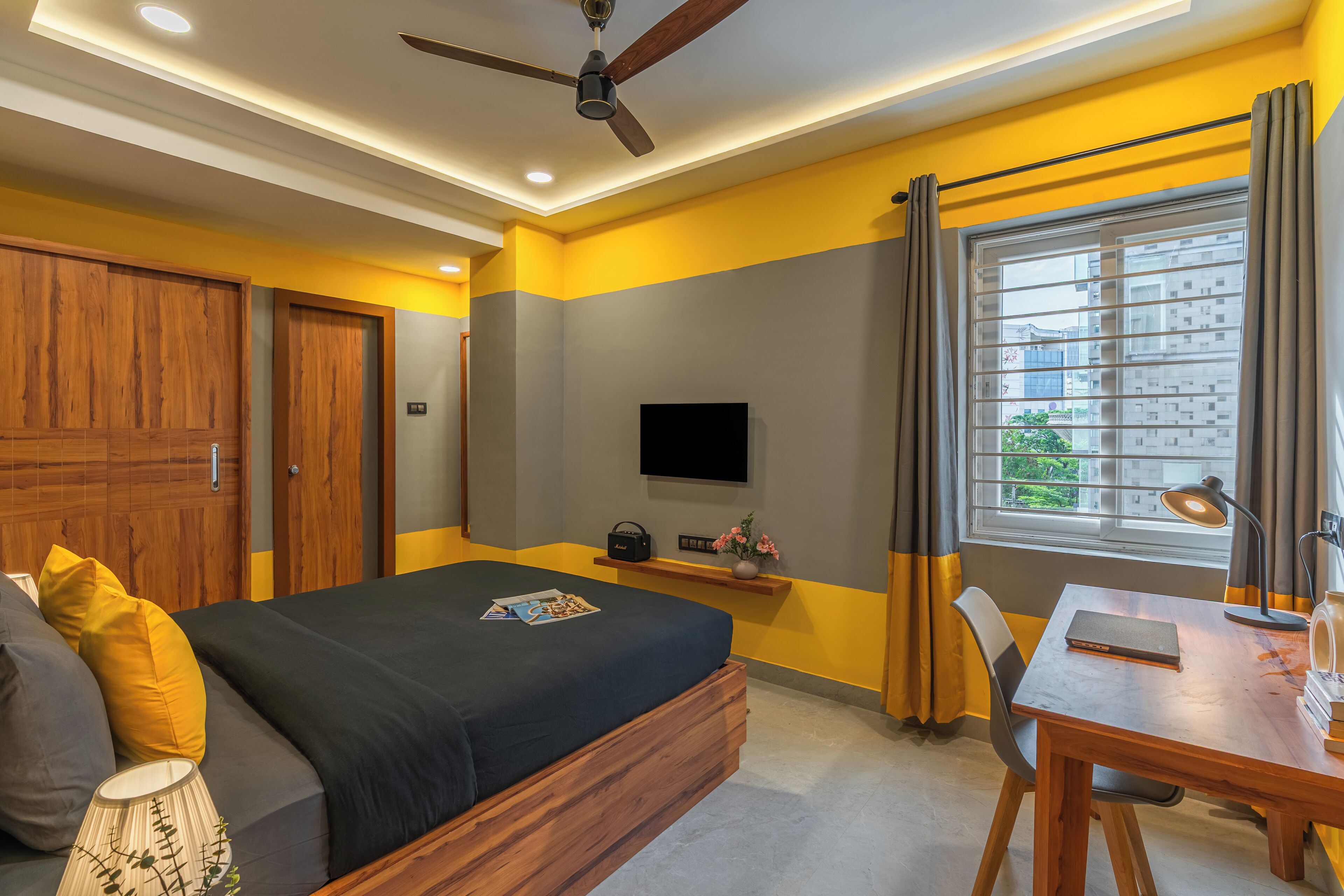 Un dormitorio con cama, escritorio, silla, televisor y ventana con cortinas.