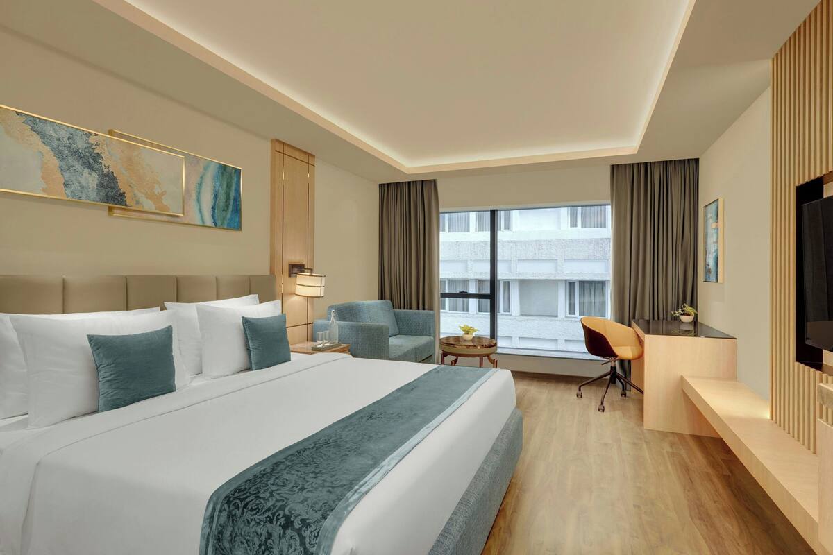 A hotel room with a large bed, a desk, a chair, a TV, and a window with curtains.