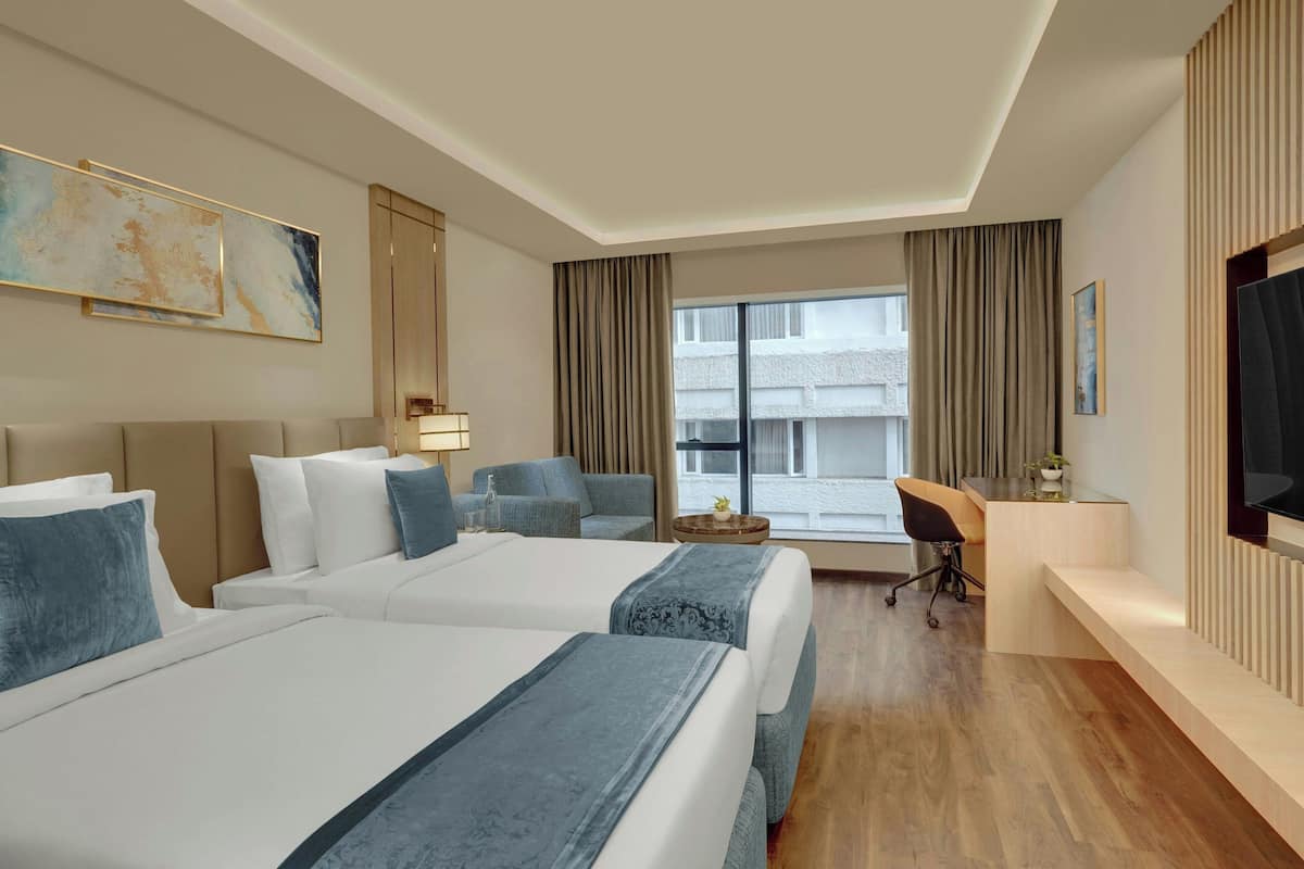 A hotel room with two beds, a desk, a chair, a TV, and a large window with curtains.