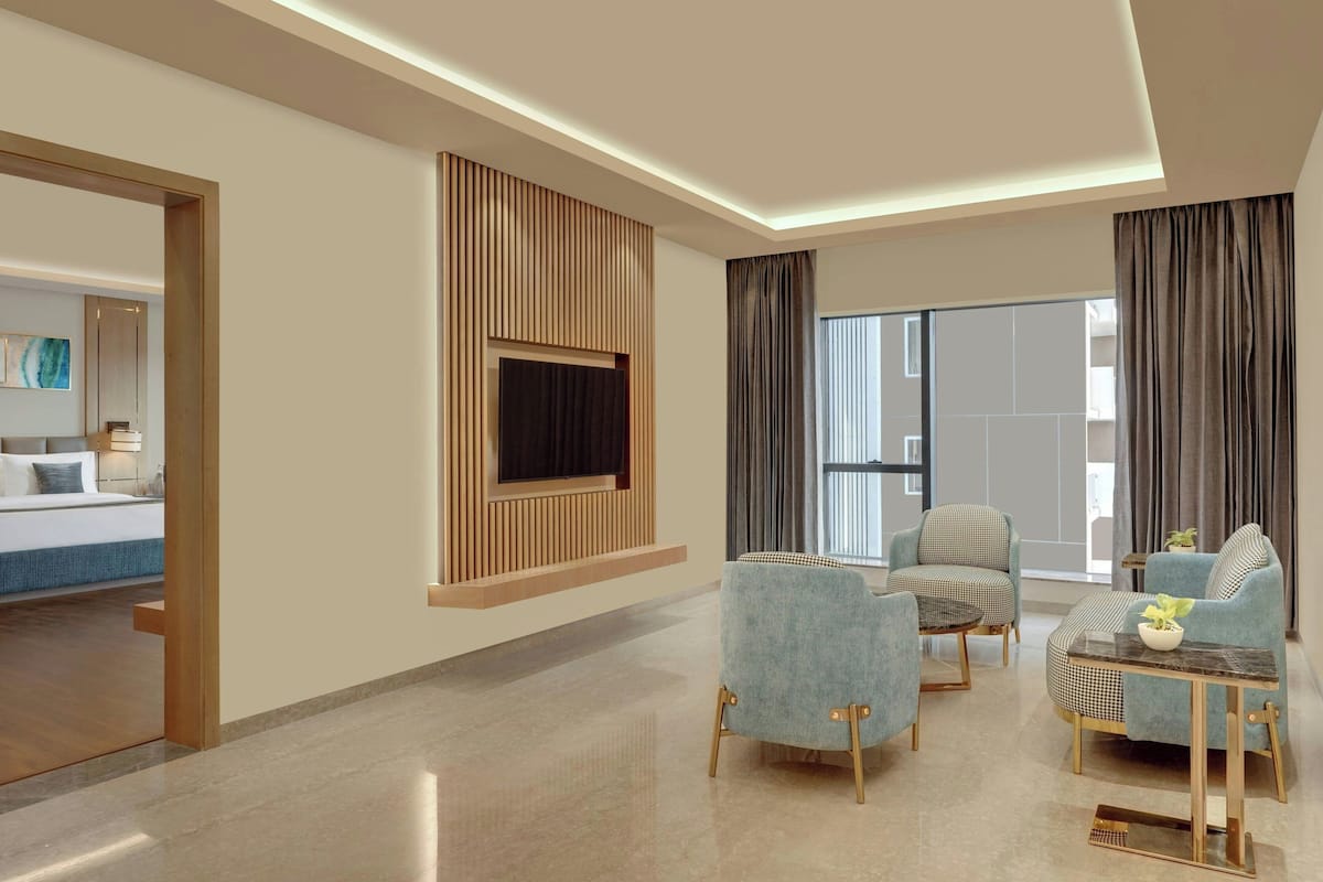 A modern living room with a flat-screen TV mounted on a wooden panel, two armchairs, a sofa, and a coffee table.