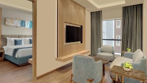 A modern hotel room with a bed, a TV mounted on a wooden panel, a seating area with a table and chairs, and a large window with curtains. - The Fern Residency Bengaluru, Seshadripuram, Series by Marriott (Bengaluru)