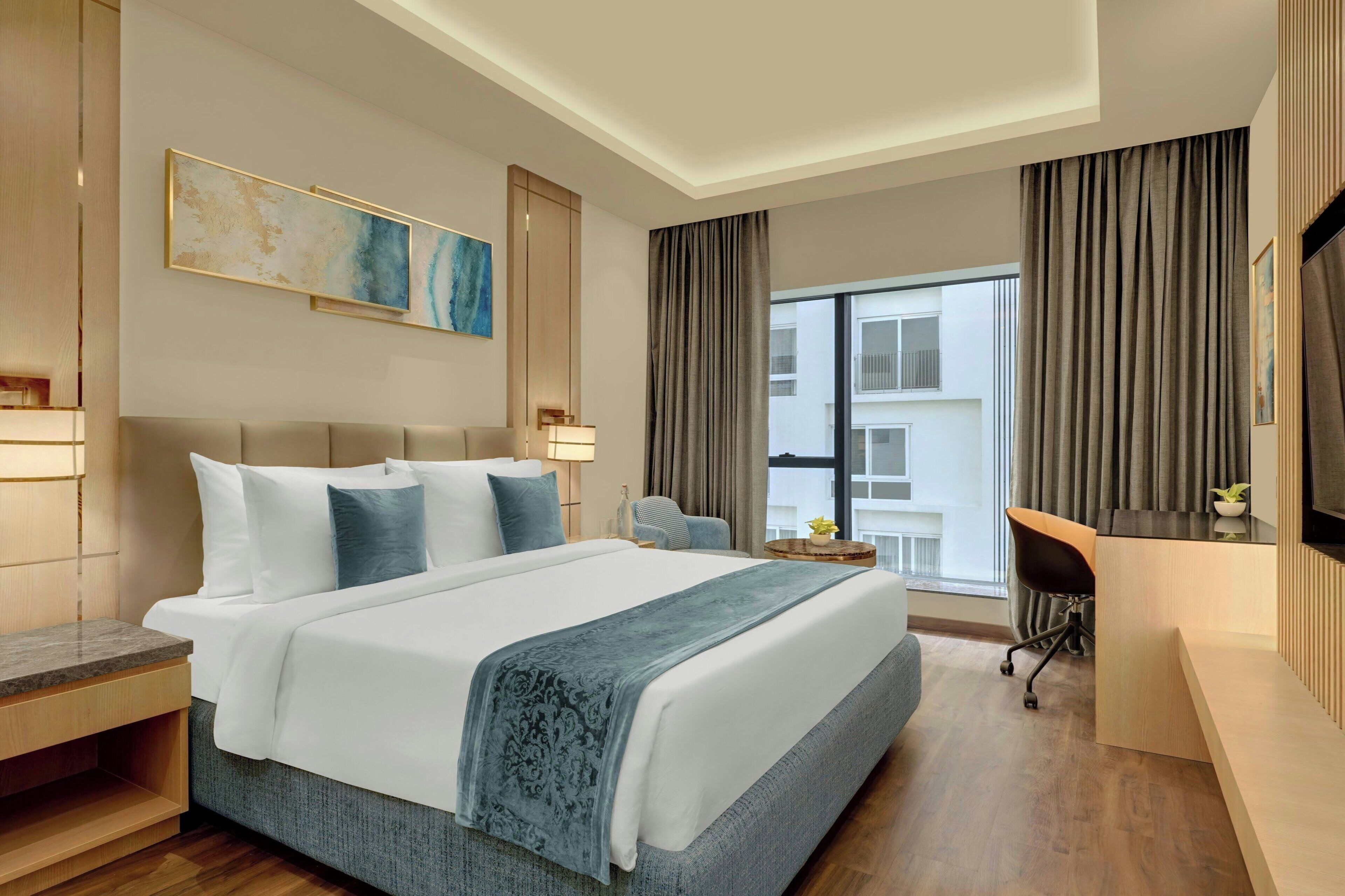 A modern hotel room with a large bed, a desk, a chair, and a TV.