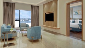 A modern hotel room with a large window, a flat-screen TV mounted on a wooden panel, a bed with blue bedding, and a seating area with blue armchairs and a small table. - The Fern Residency Bengaluru, Seshadripuram, Series by Marriott (Bengaluru)
