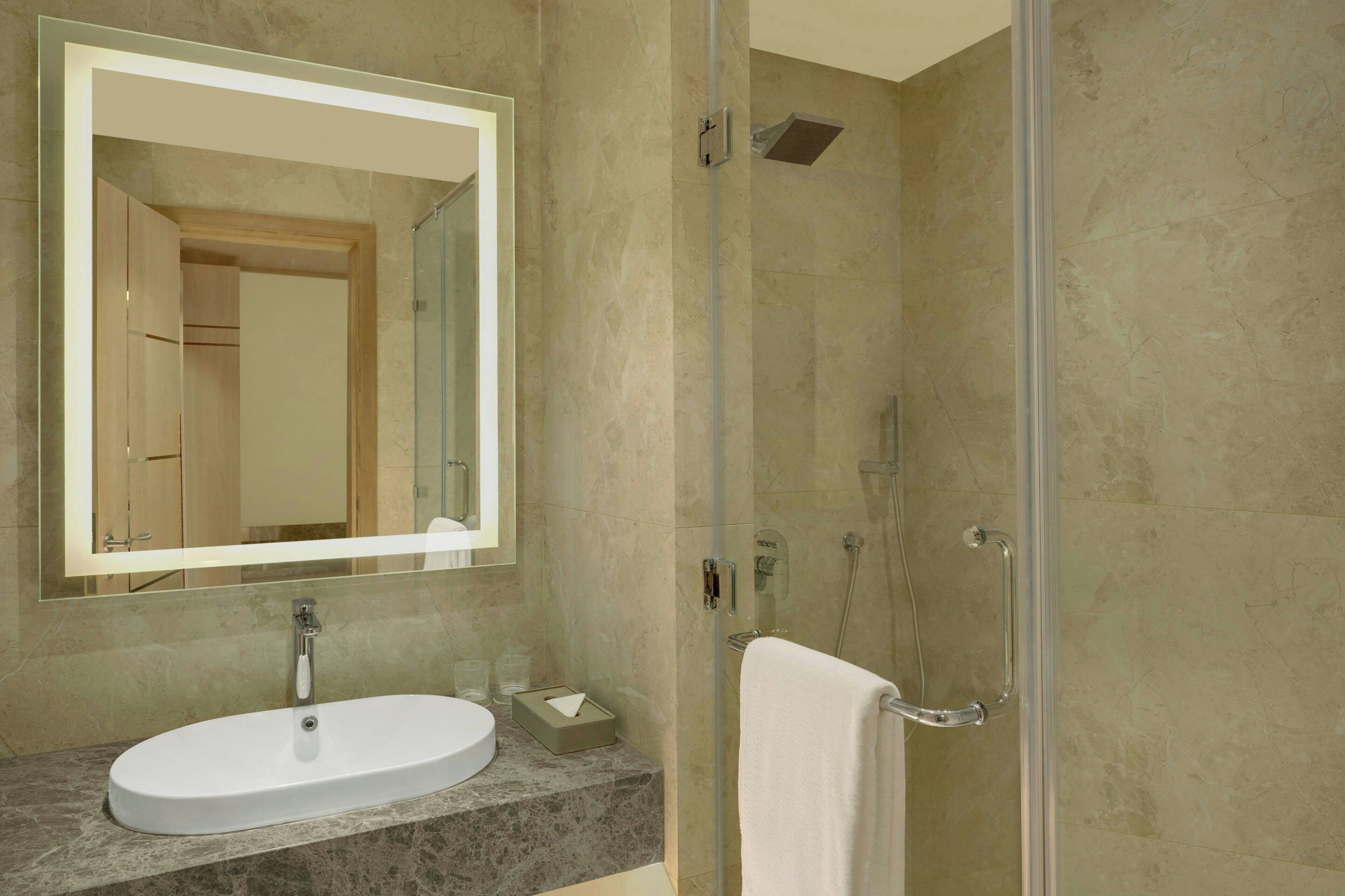 Un baño moderno con un lavamanos ovalado grande, un espejo y una cabina de ducha con paredes de vidrio.