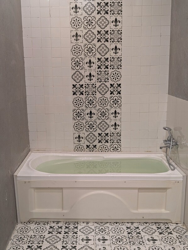 A bathroom with a white bathtub, black and white patterned tiles on the walls, and a shower area. - Qila Hotel (Moradabad)