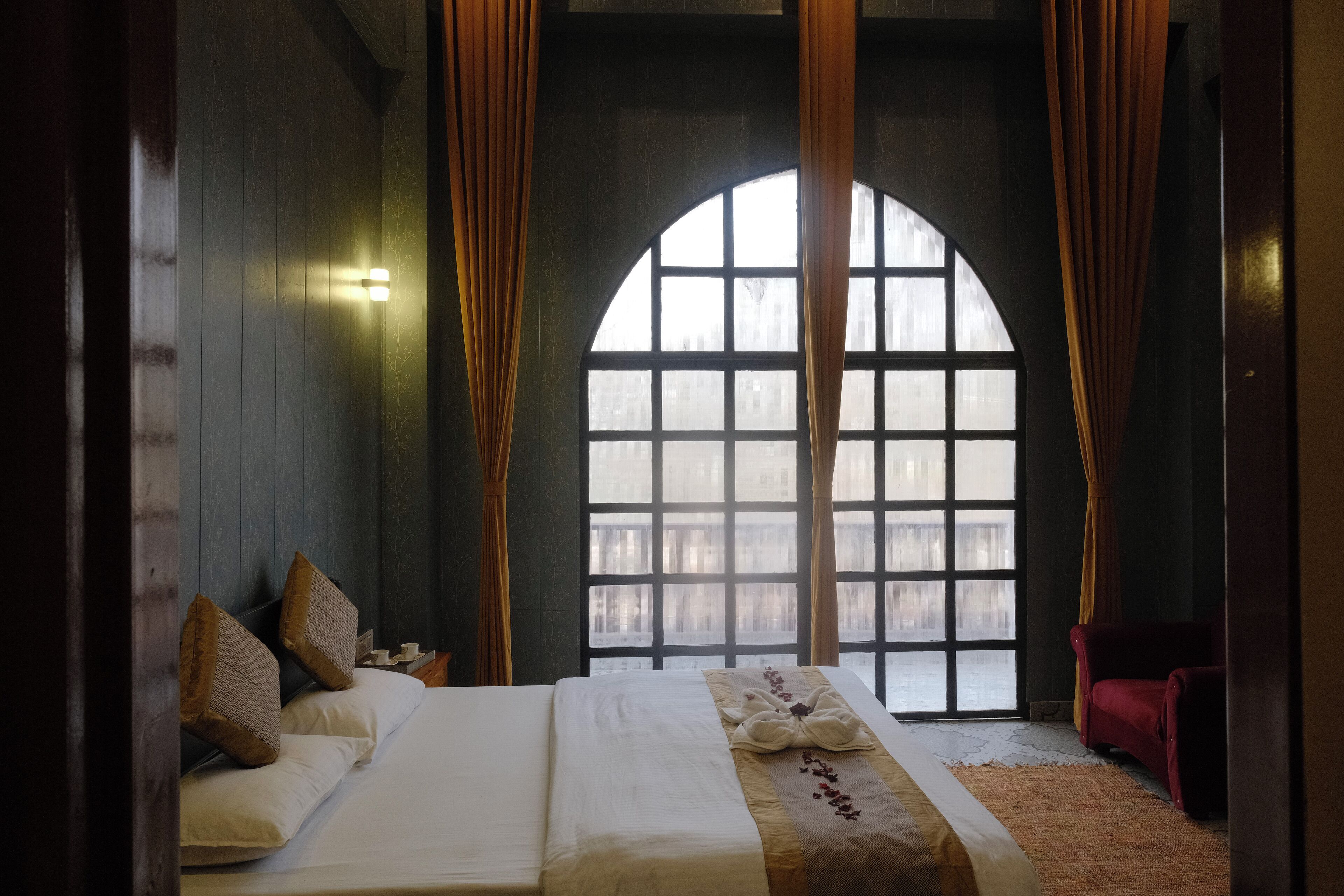 Una habitación con un gran ventanal arqueado, una cama con ropa de cama blanca y una silla roja.