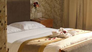 A neatly made bed with white linens and a decorative gold and brown bedspread. There is a wooden nightstand with a vase of flowers and a book beside the bed.