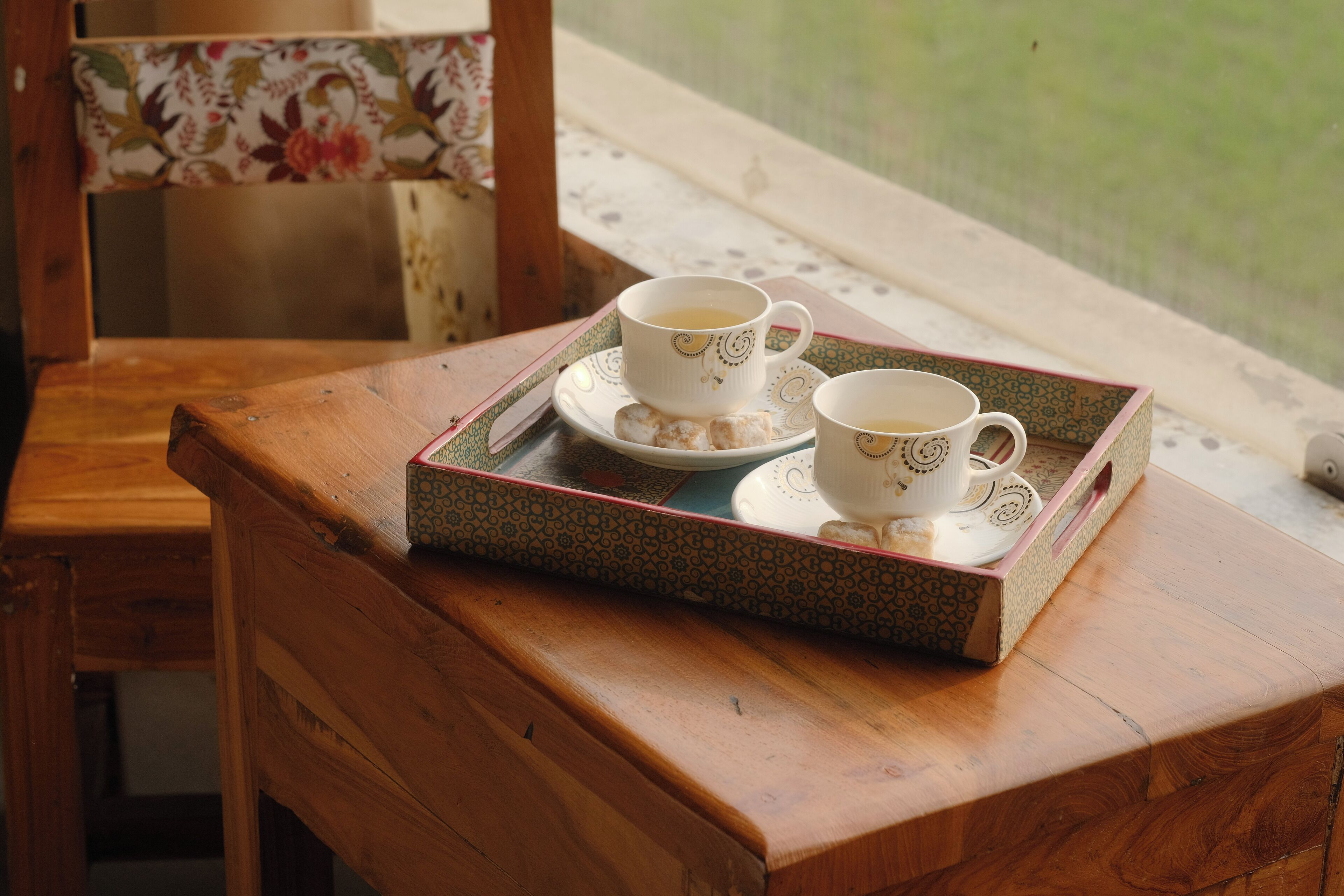 A wooden table with a tray holding two cups and a saucer, placed on a window sill.