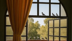 A room with a glass table, red sofas, and a view of birds on a balcony. - Qila Hotel (Moradabad)