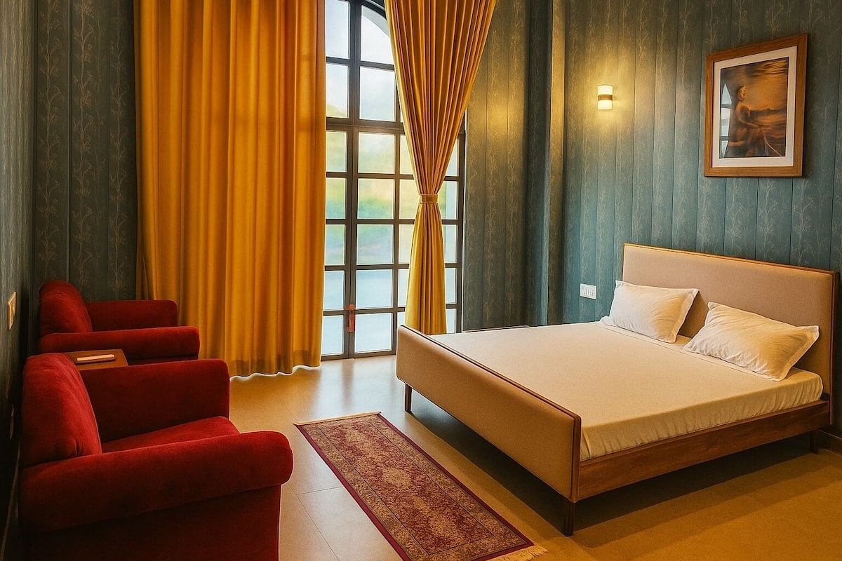 A hotel room with a bed, red chairs, a window with curtains, and a painting on the wall.
