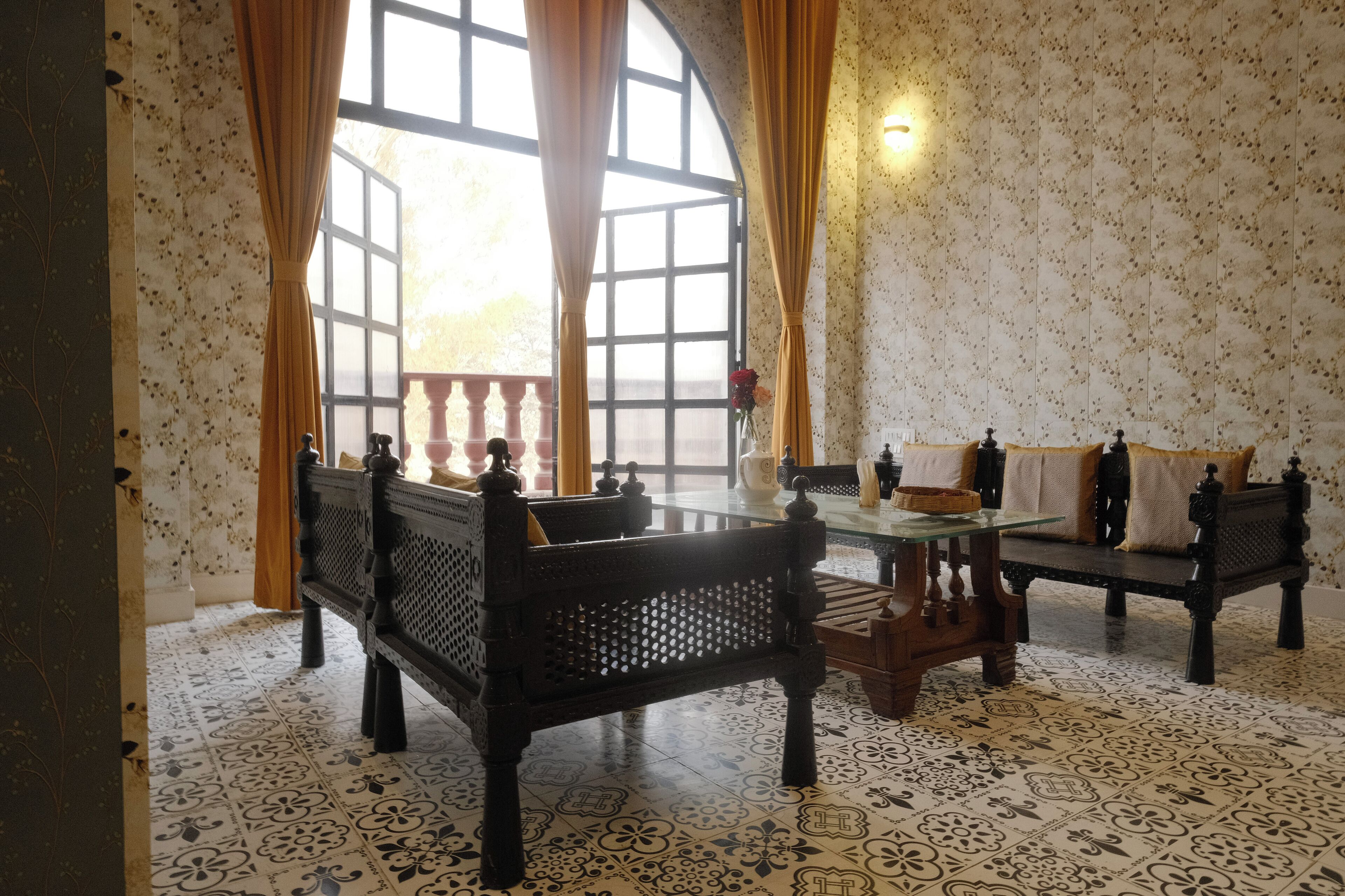 A room with a large arched window, two wooden benches, a glass table, and patterned floor tiles.