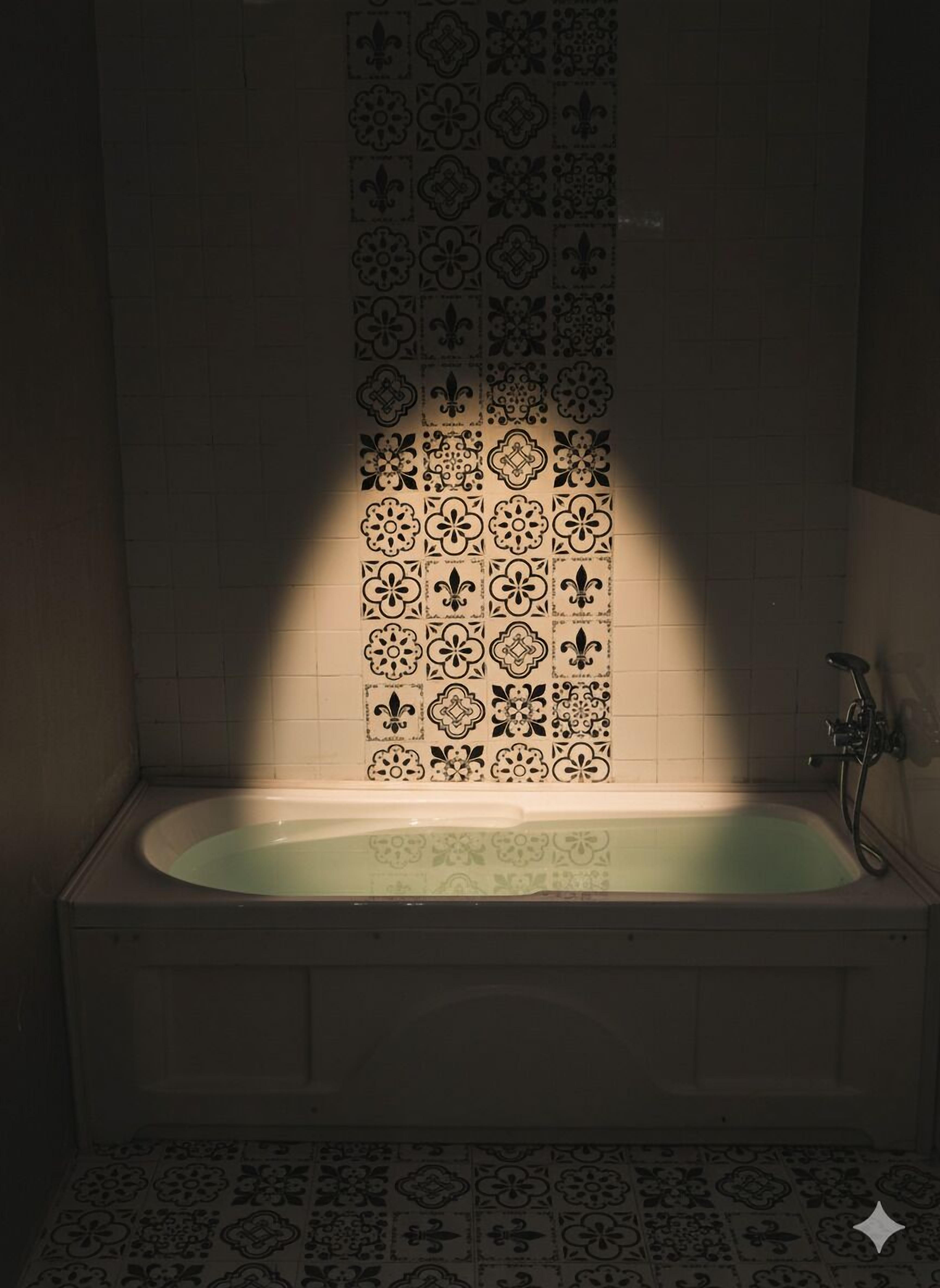 A bathtub with a patterned tile wall behind it.