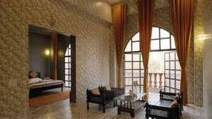 A room with a bed, a sofa, a coffee table, and a window with curtains. - Qila Hotel (Moradabad)