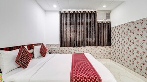 A hotel room with a bed, white walls, a floral-patterned wallpaper, a red and white bedspread, and a window with curtains. - Hotel Amour By RMR Hotels (New Delhi)