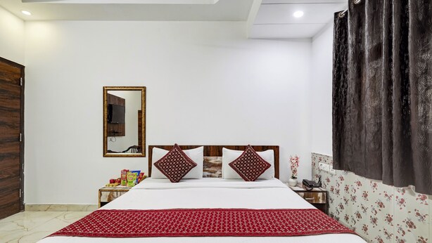 A bedroom with a large bed, a wooden headboard, a nightstand with a lamp, a mirror, and a wardrobe. - Hotel Amour By RMR Hotels (New Delhi)