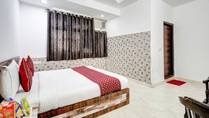 A bedroom with a bed, a window with curtains, a door, and a small rug. - Hotel Amour By RMR Hotels (New Delhi)