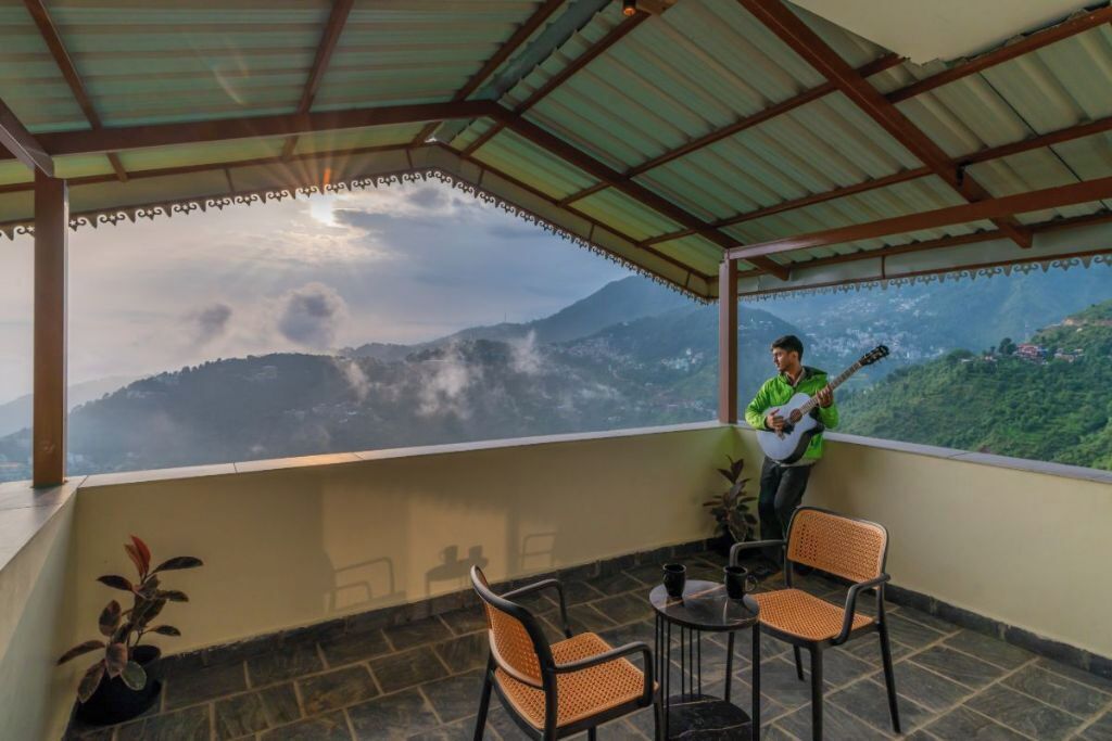 A balcony with a view of mountains, a person playing a guitar, and two wicker chairs.