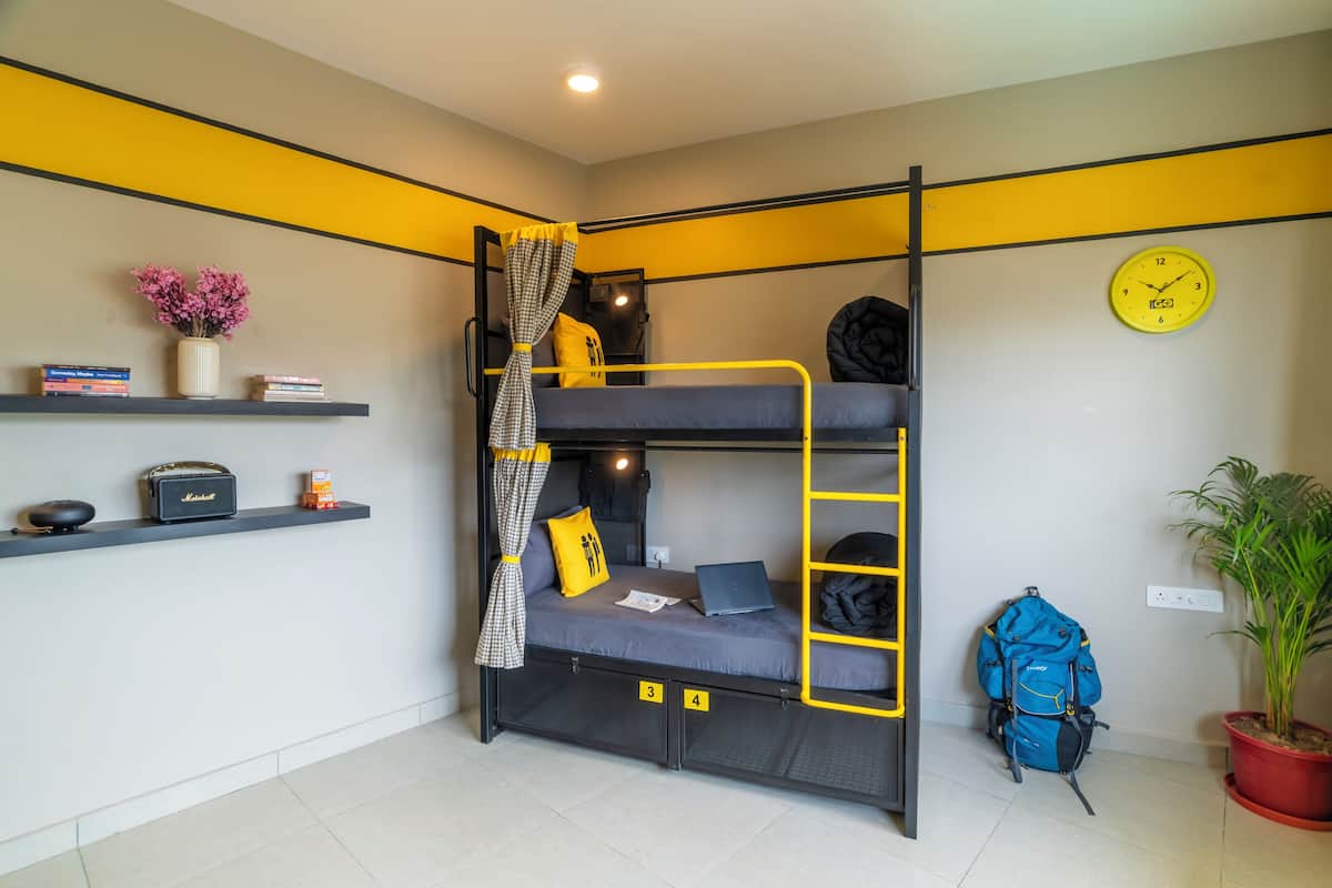 Une chambre avec un lit superposé, une étagère où sont posés des livres, une lampe et un vase avec des fleurs.