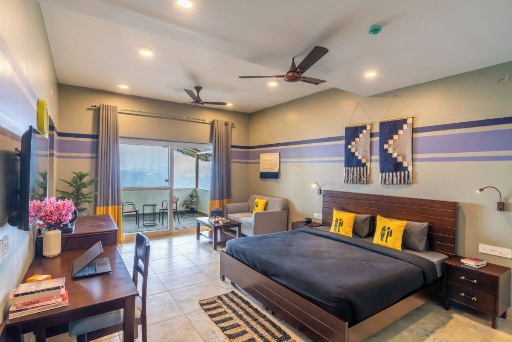 A bedroom with a bed, desk, chairs, and a balcony.